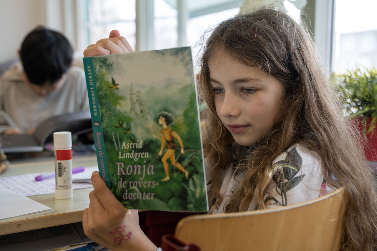 Meisje met lange blonde haren leest in Ronja en de Roversdochter van Astrid Lindgren