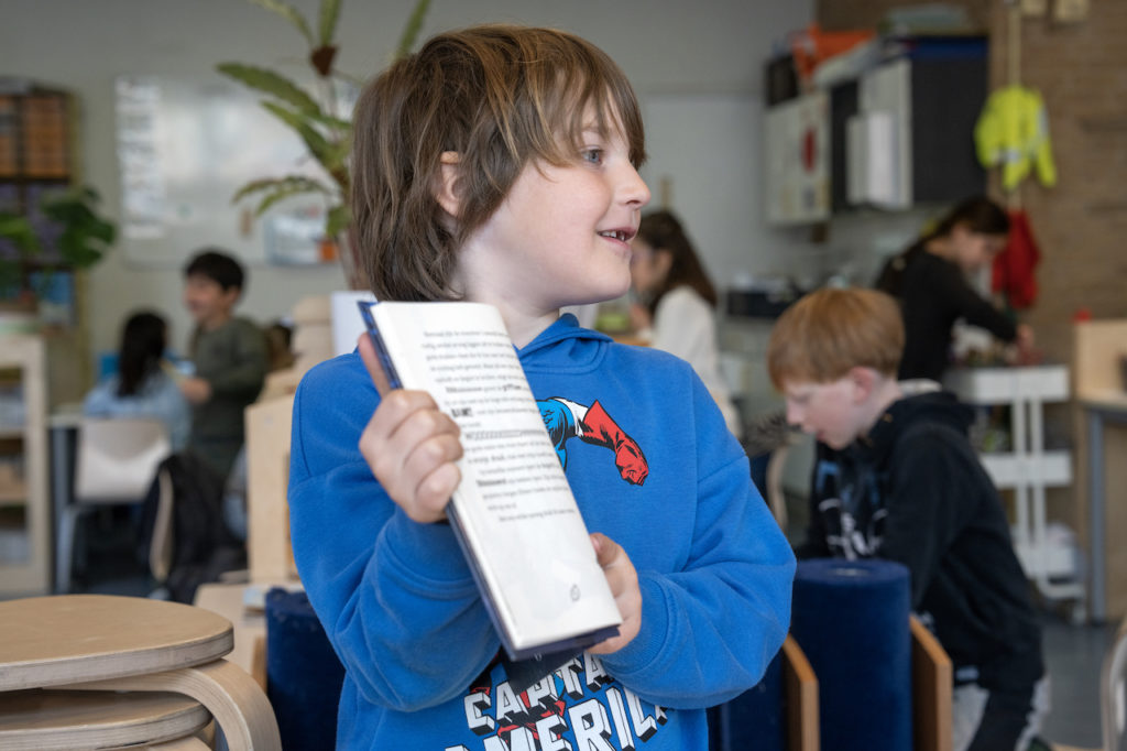 Jongen die een leesboek omhoog houdt om het te laten zien aan een ander die niet in beeld is. 