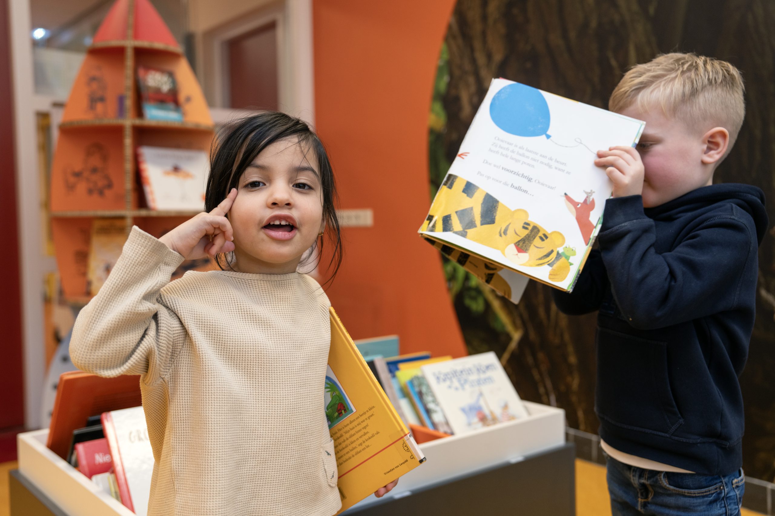 Kinderen met prentenboeken in de hand, links kijkt het kind in de camera, rechts staat een kind in een boek te kijken.