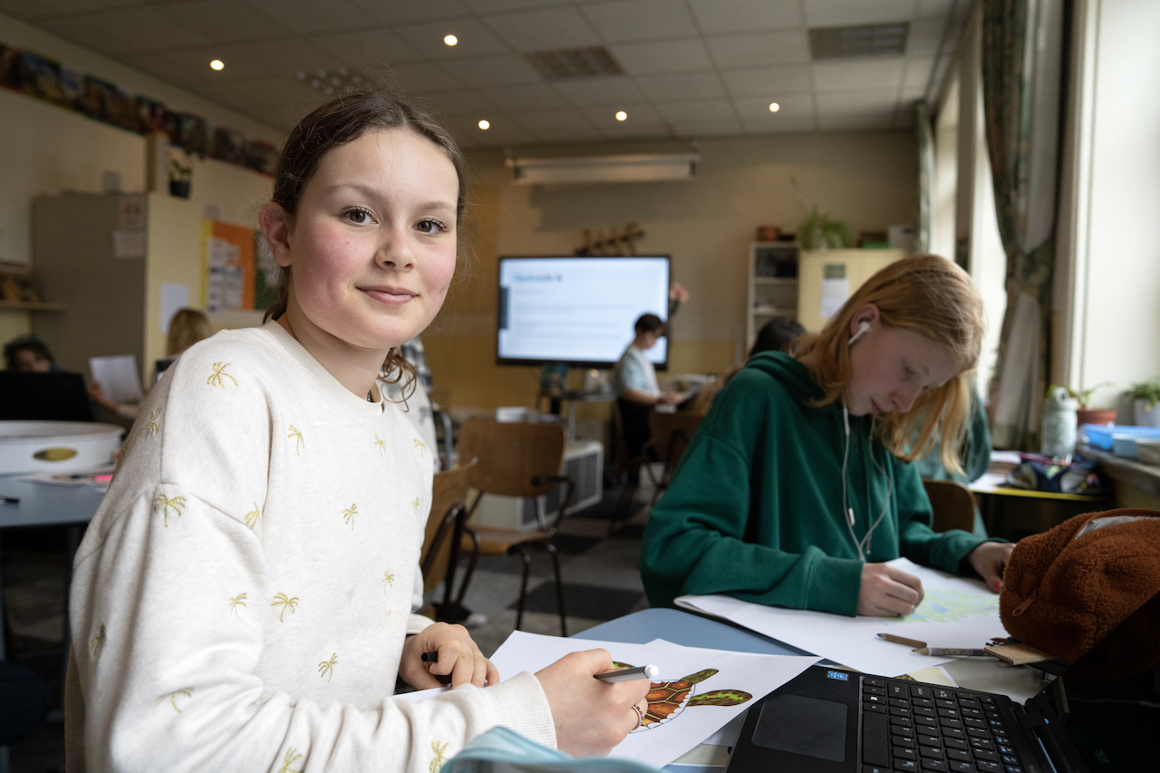 Leerling kijkt de camera in terwijl ze samen met een klasgenoot aan een opdracht werkt - Rijke thema's