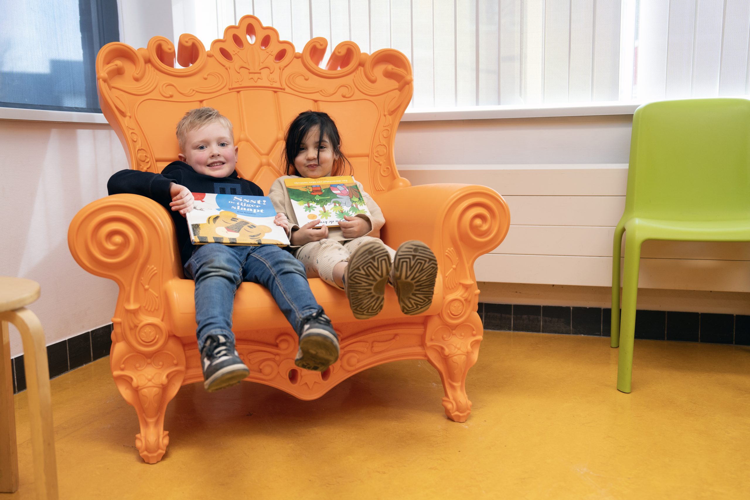 Twee kleuters in een grote oranje voorleesstoel met een prentenboek op hun schoot. 